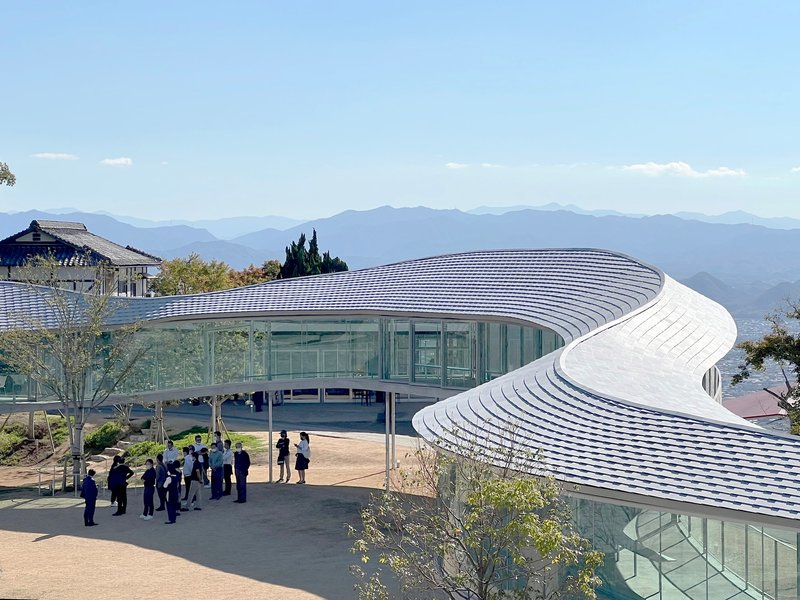 Ribbed white roof canopy over continuous glass walls with visitors gathered on the forecourt