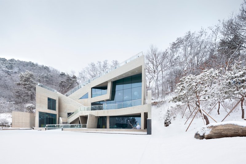 Angular concrete volumes with cantilevered upper floors and full-height glazing set into a snowy hillside