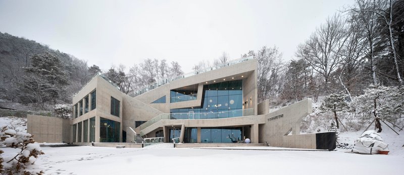 Frontal view of the concrete facade with interlocking volumes and ribbon windows under overcast winter sky