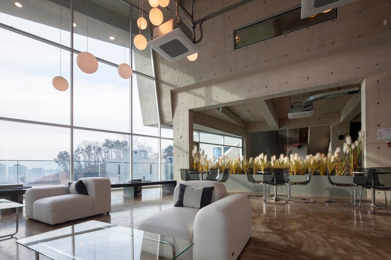 Double-height lobby with concrete ceiling, floor-to-ceiling glazing and pendant lighting above seating
