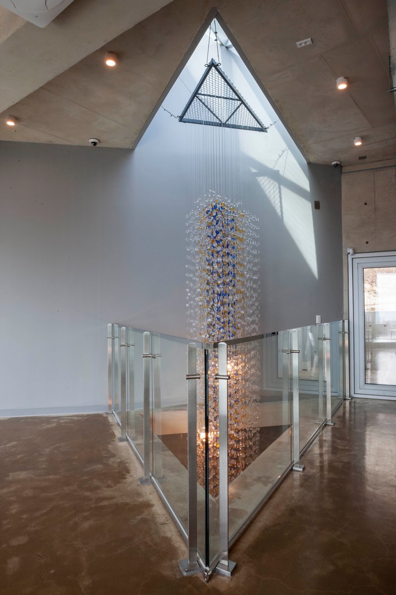 Double-height space with triangular skylight above a glass-railed stair opening and cascading chandelier