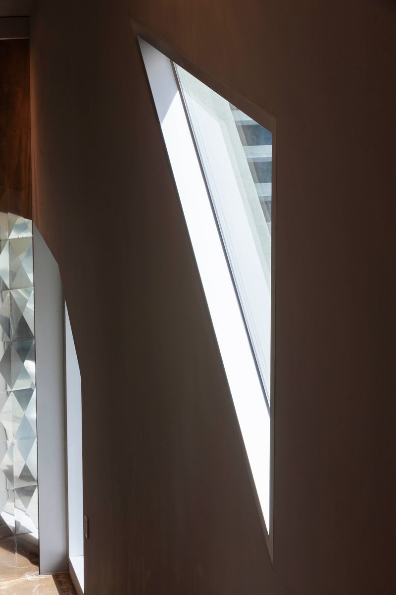 Angled skylight slicing through a dark interior wall with daylight spilling onto the floor