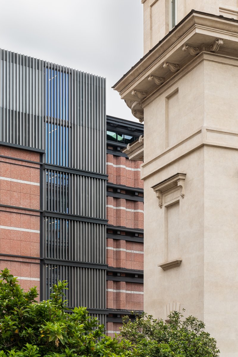 Vertical fin louvres rising beside red brick bands and a rendered heritage corner under overcast skies
