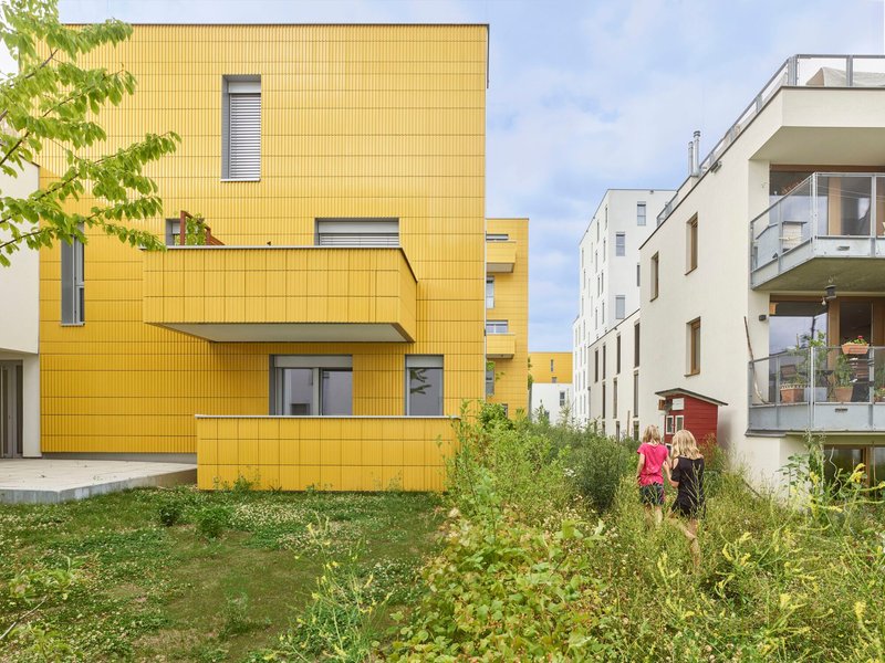 Yellow corrugated metal facade with cantilevered balcony and green planting in the courtyard below