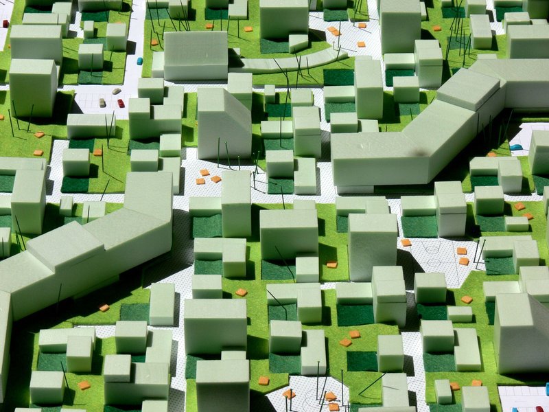 Physical model showing massing arrangement with green foam volumes, white paved surfaces, and small orange accent pieces