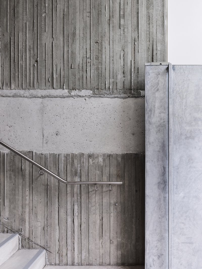 Board-formed concrete wall with stainless steel handrail alongside white painted masonry wall