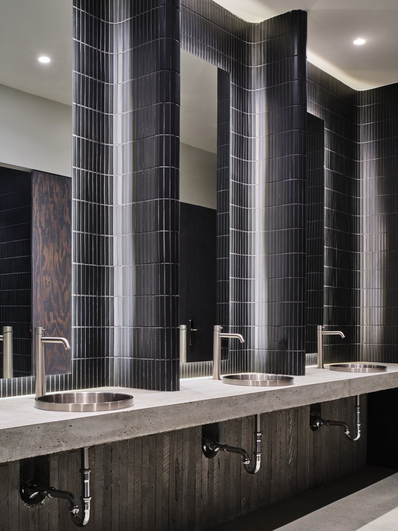 Restroom vanity with terrazzo counter, round metal sinks and vertically ribbed black tile wall panels