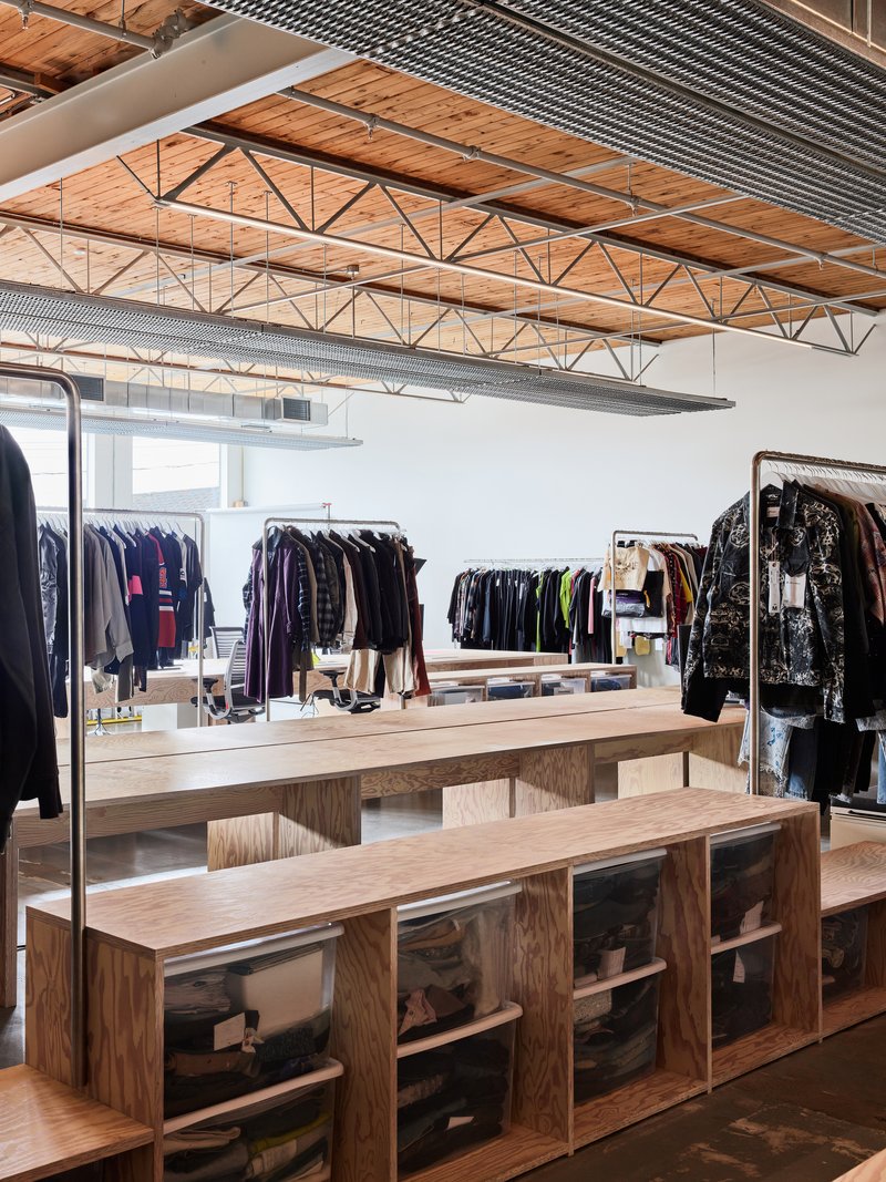 Open retail area with exposed wood trusses, metal deck ceiling and plywood display benches beneath clothing racks