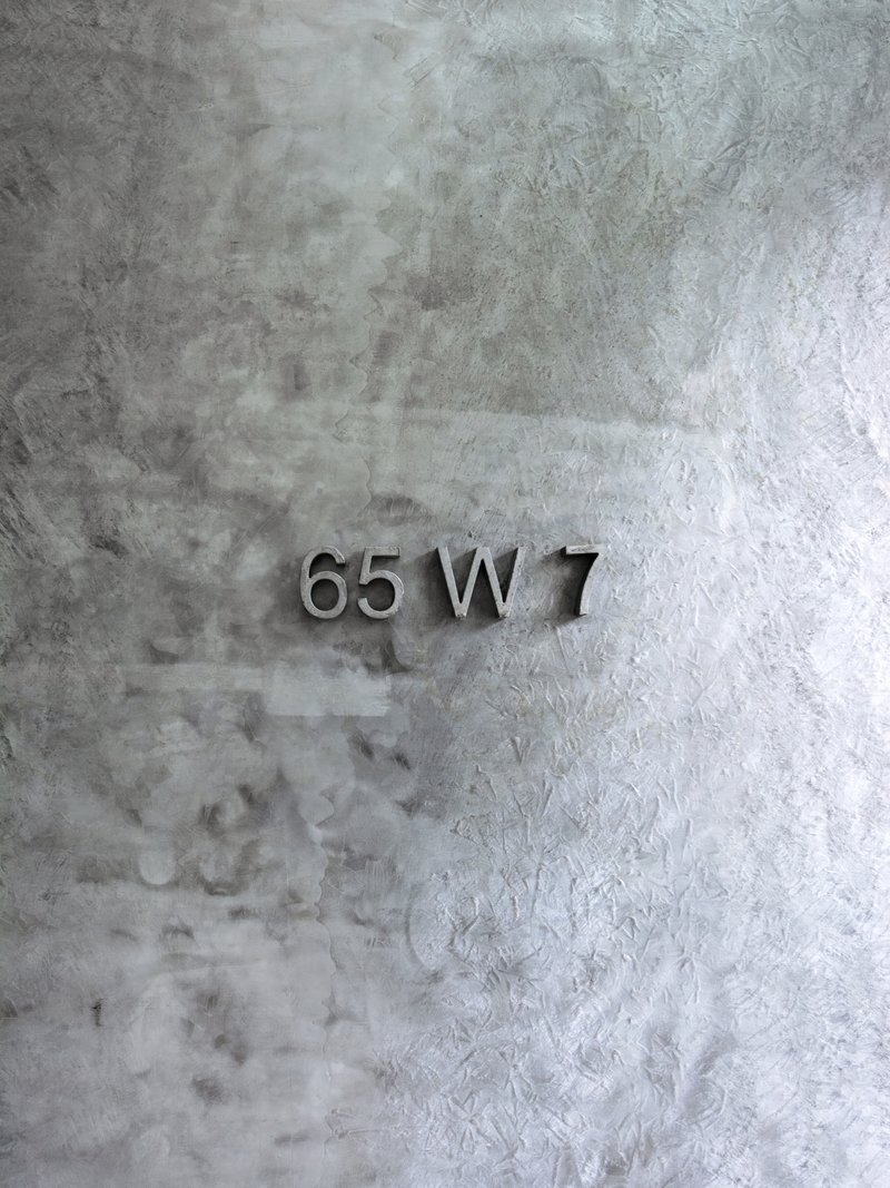 Metallic address numbers mounted on a textured concrete wall with weathered patina