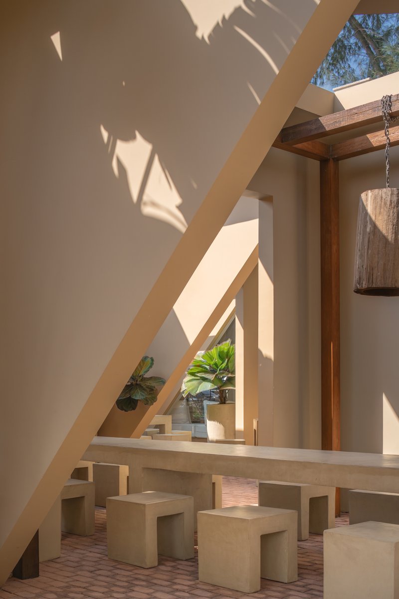 Angular wall casting shadow over a raised dining platform with benches beneath a skylight and timber beams