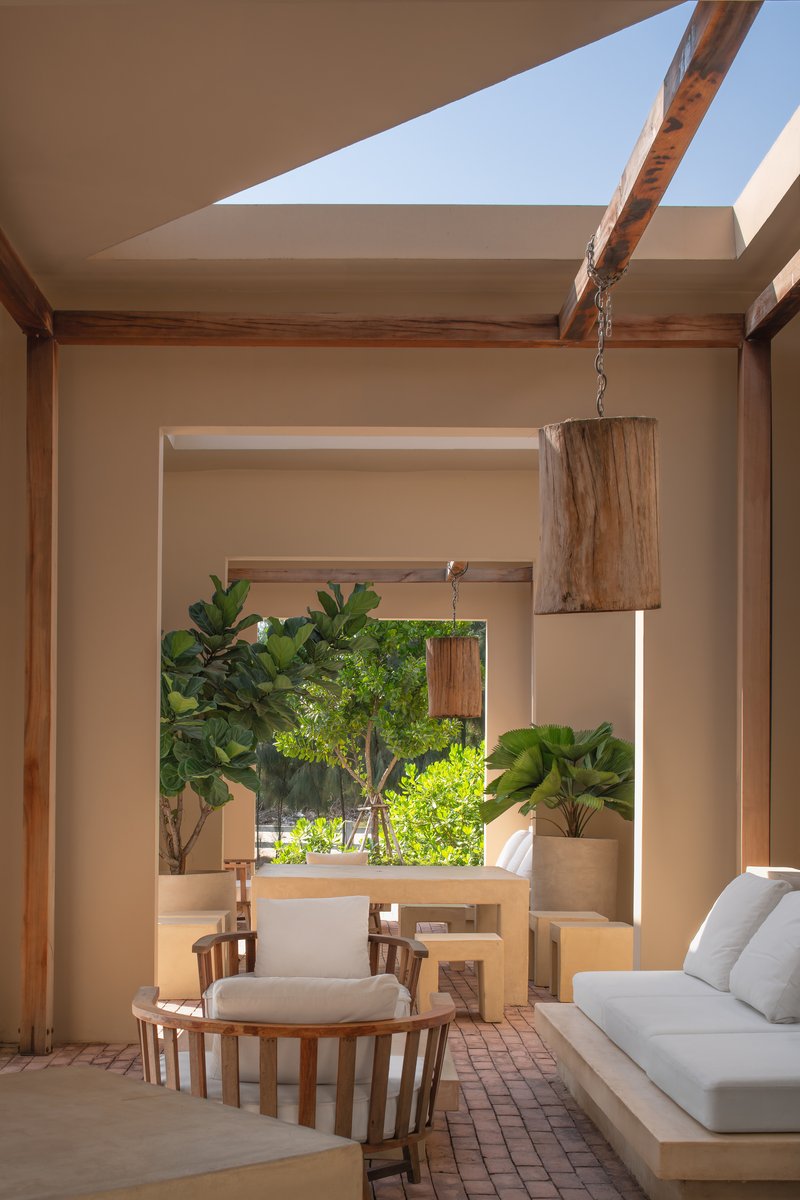 Framed view through sequential openings to a planted courtyard with suspended timber light fixture