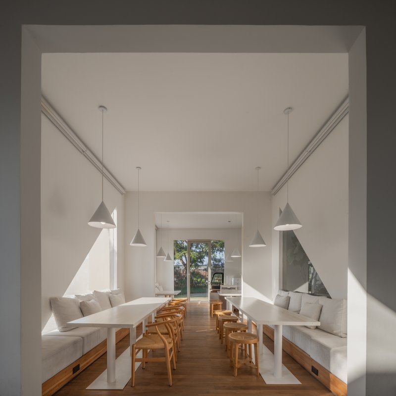 White dining room with built-in benches, timber chairs and pendant lights casting triangular shadows
