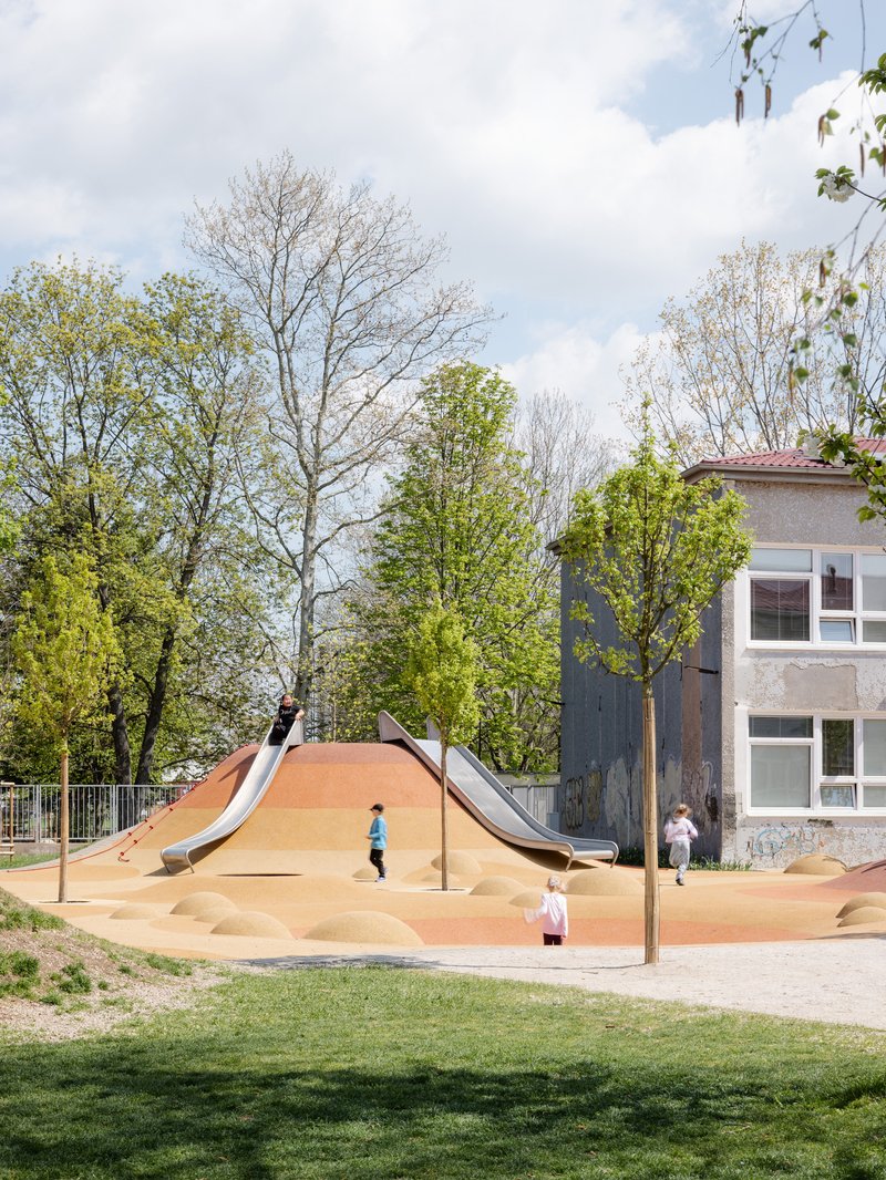 Play area with twin slides on a sand dune and children moving between young trees