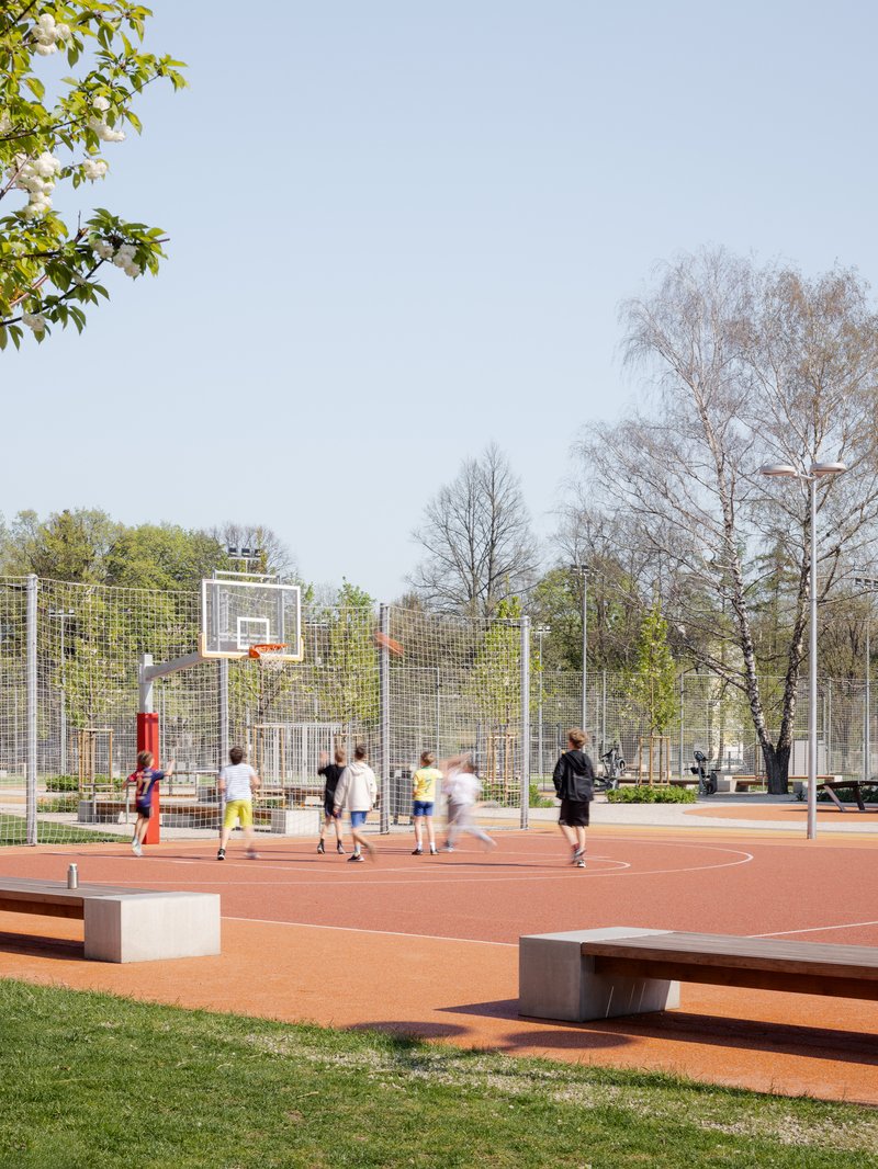 Basketball court with wire mesh fencing and children playing under spring foliage