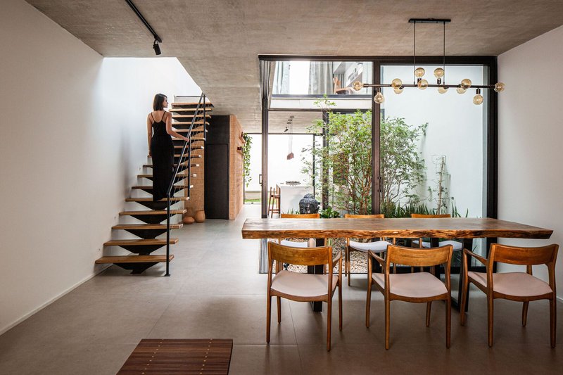 Dining area with live-edge wood table and cantilevered timber staircase alongside a courtyard window