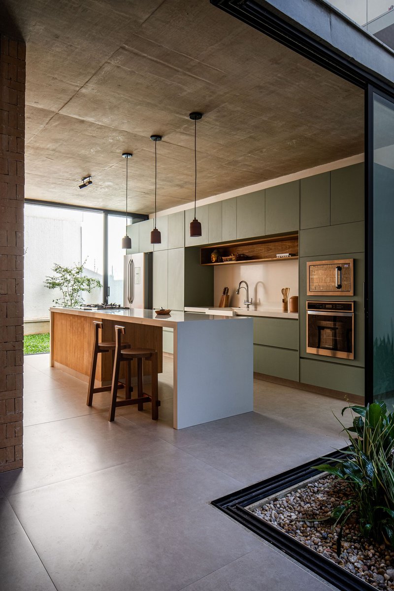 Kitchen with sage green cabinetry, timber island and pendant lights under exposed concrete ceiling