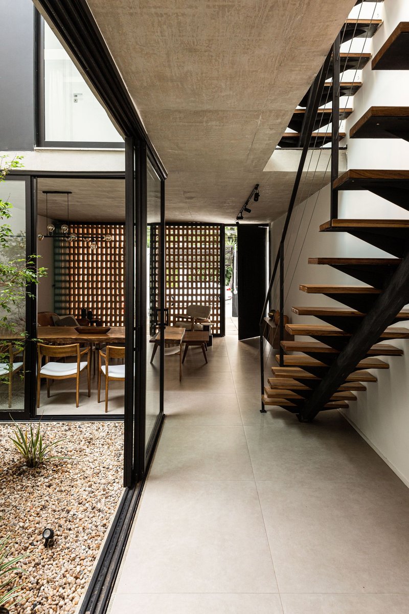 Open-tread staircase with steel stringers and glass railing beside glazed courtyard wall