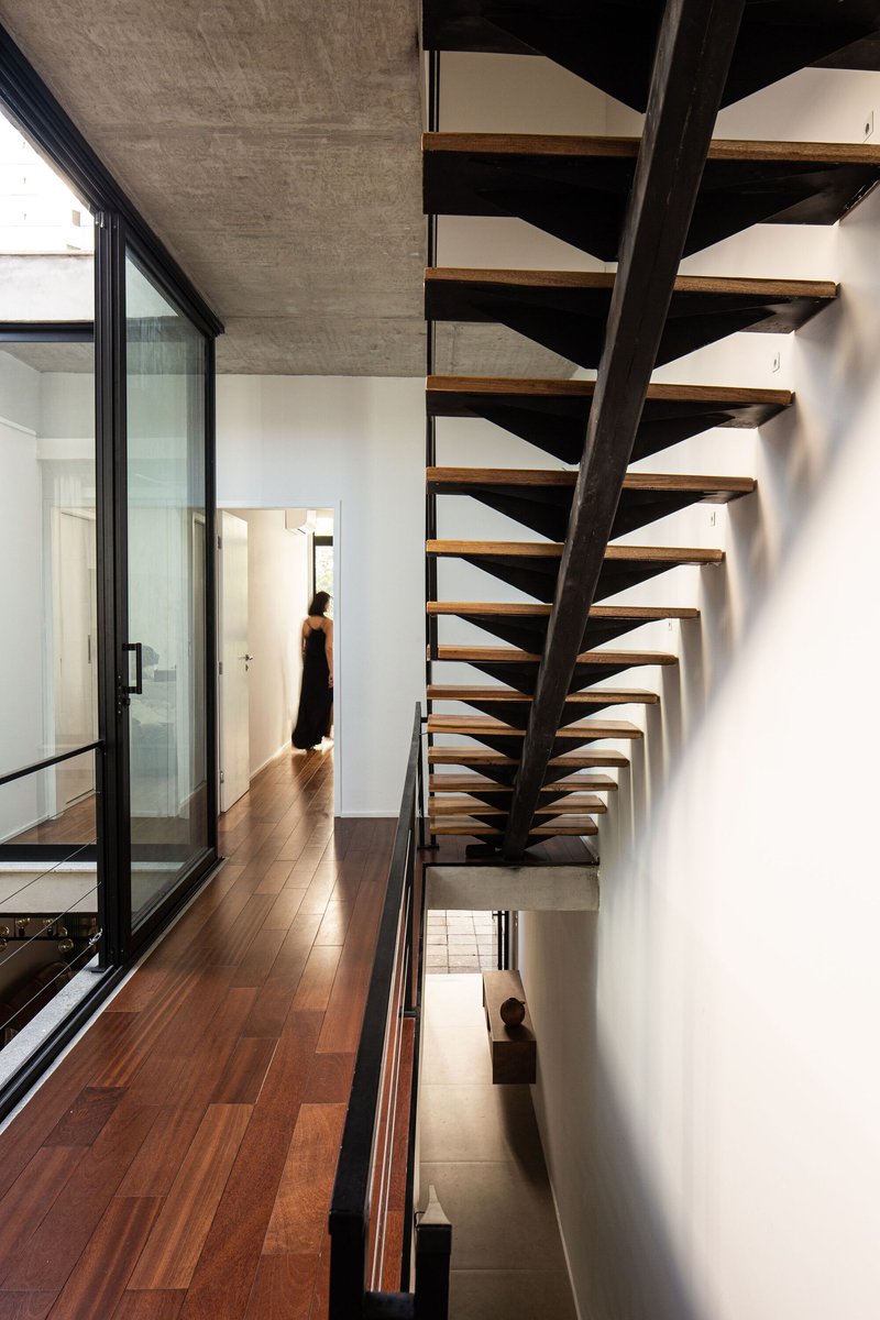 Open timber tread staircase with black steel spine ascending through triple-height space