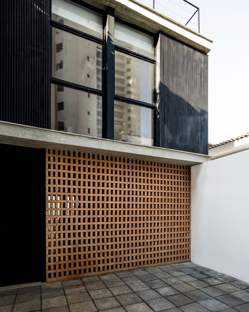 Perforated brick screen beneath a concrete slab and corrugated metal upper level against overcast sky