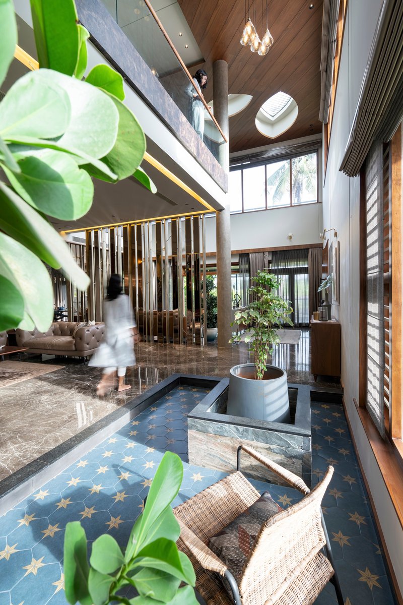 Double-height interior with patterned tile floor, timber ceiling panels, and a person descending the staircase