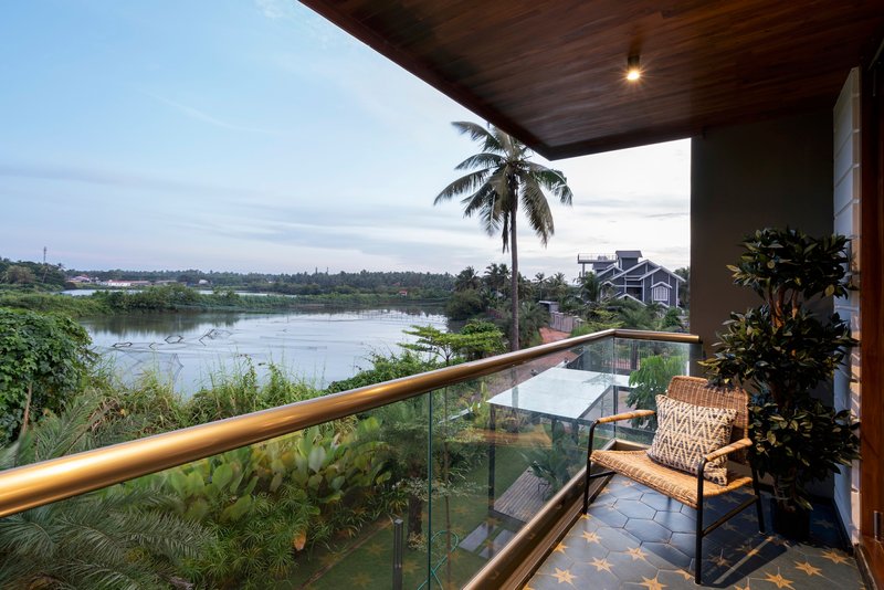 Covered balcony with timber soffit and glass railing overlooking a palm-lined river at dusk