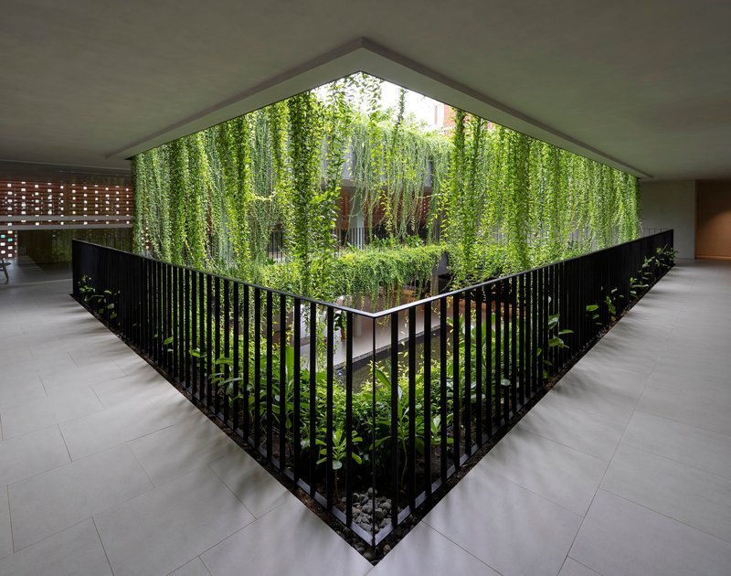 Triangular interior courtyard with black vertical railings enclosing a planted garden and cascading greenery above