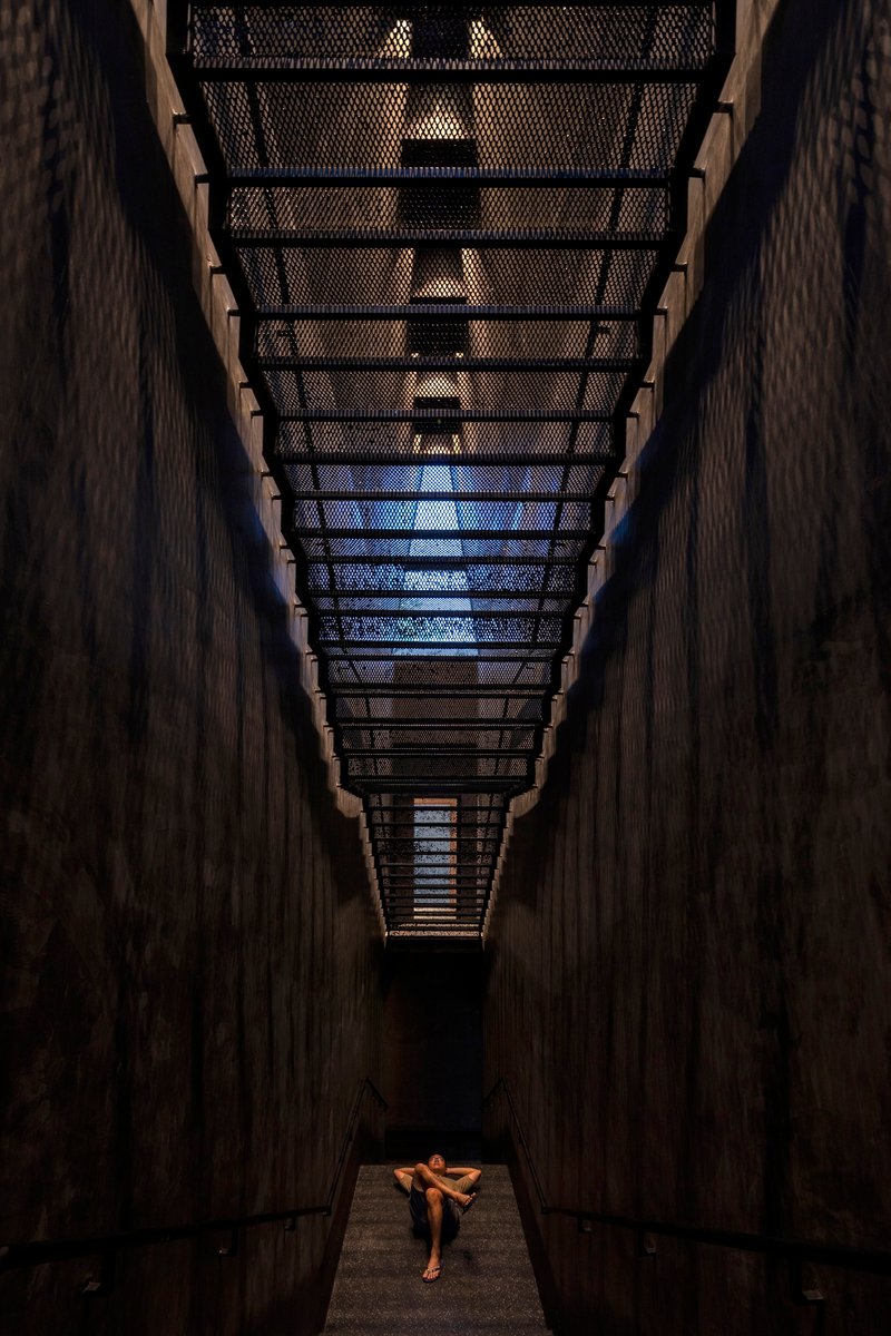Upward view of narrow skylight with perforated metal screen and timber walls framing a figure below