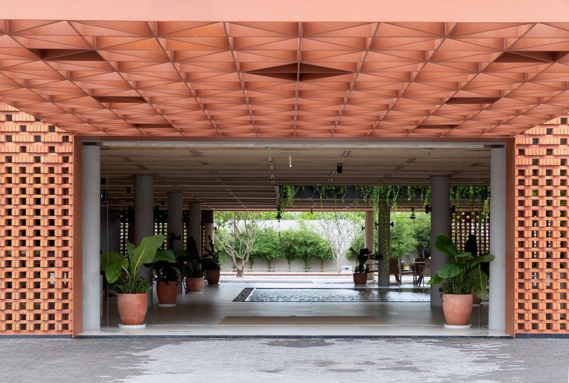 Covered entry passage with geometric timber ceiling and open brick screens flanking potted plants