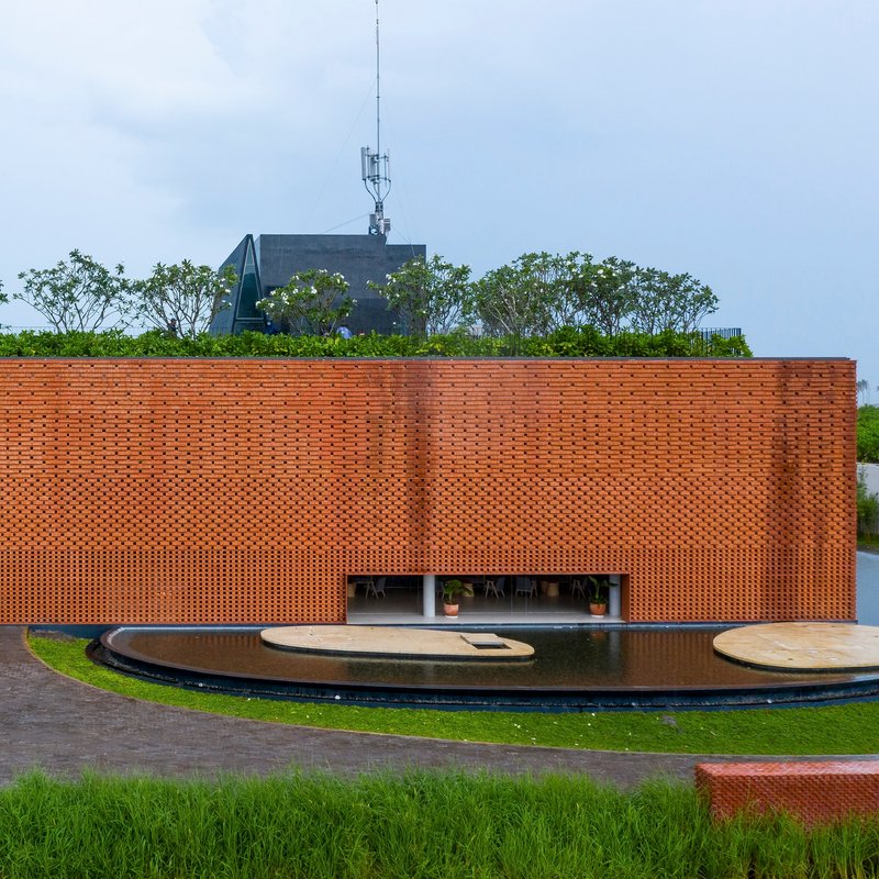 Perforated terracotta brick facade with rooftop garden and curved water feature in front lawn