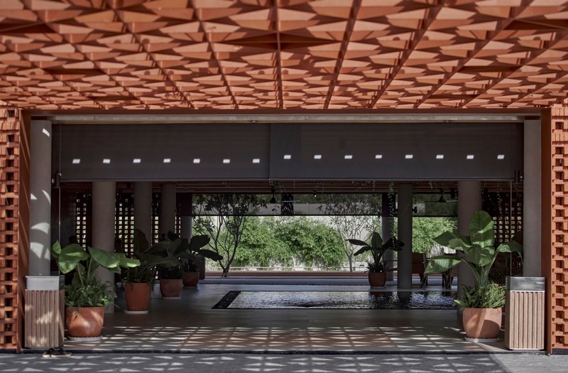 Interior view through covered entry showing perforated timber ceiling and dappled sunlight patterns