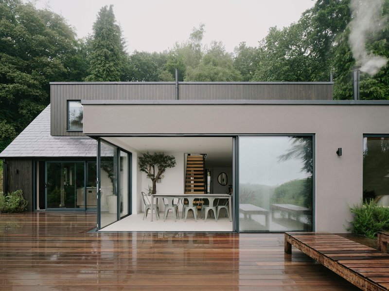 Open glass doors connecting the dining area to a wet timber deck under misty skies