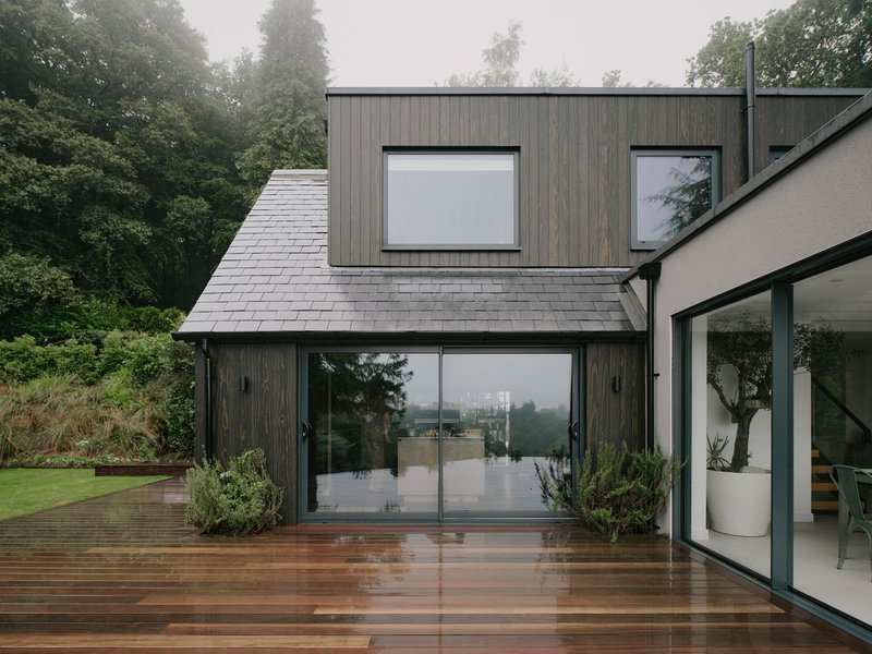 Gable volume with slate roof and timber cladding opening onto rain-soaked timber decking