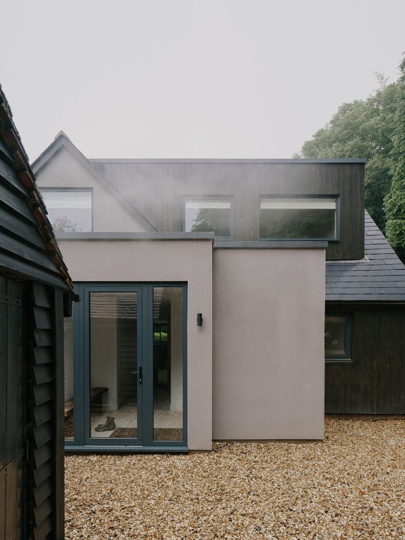 Courtyard view of timber-clad and rendered volumes with glazed entrance on a gravel surface