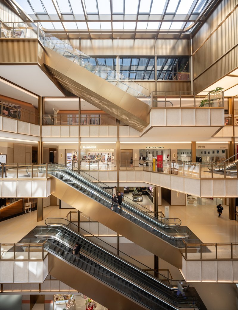 Multi-level atrium interior with escalators connecting floors beneath glazed roof and timber-clad balconies
