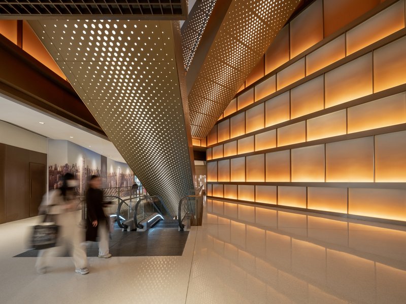 Interior corridor with perforated metal column and backlit horizontal panel wall as blurred figures pass by