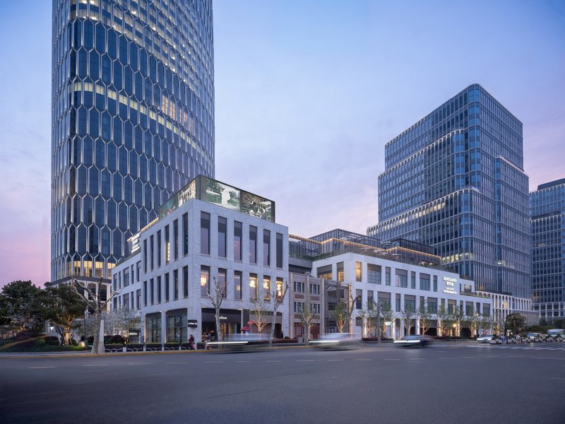 Street view of white framed podium and glass towers at dusk with blooming trees along the sidewalk
