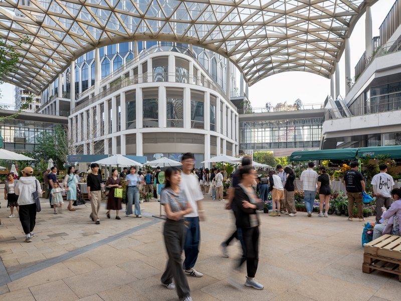 Covered market plaza with timber space frame roof and crowds moving through vendor stalls below