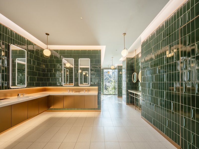 Restroom interior with green glazed tile walls and timber vanity under cove lighting