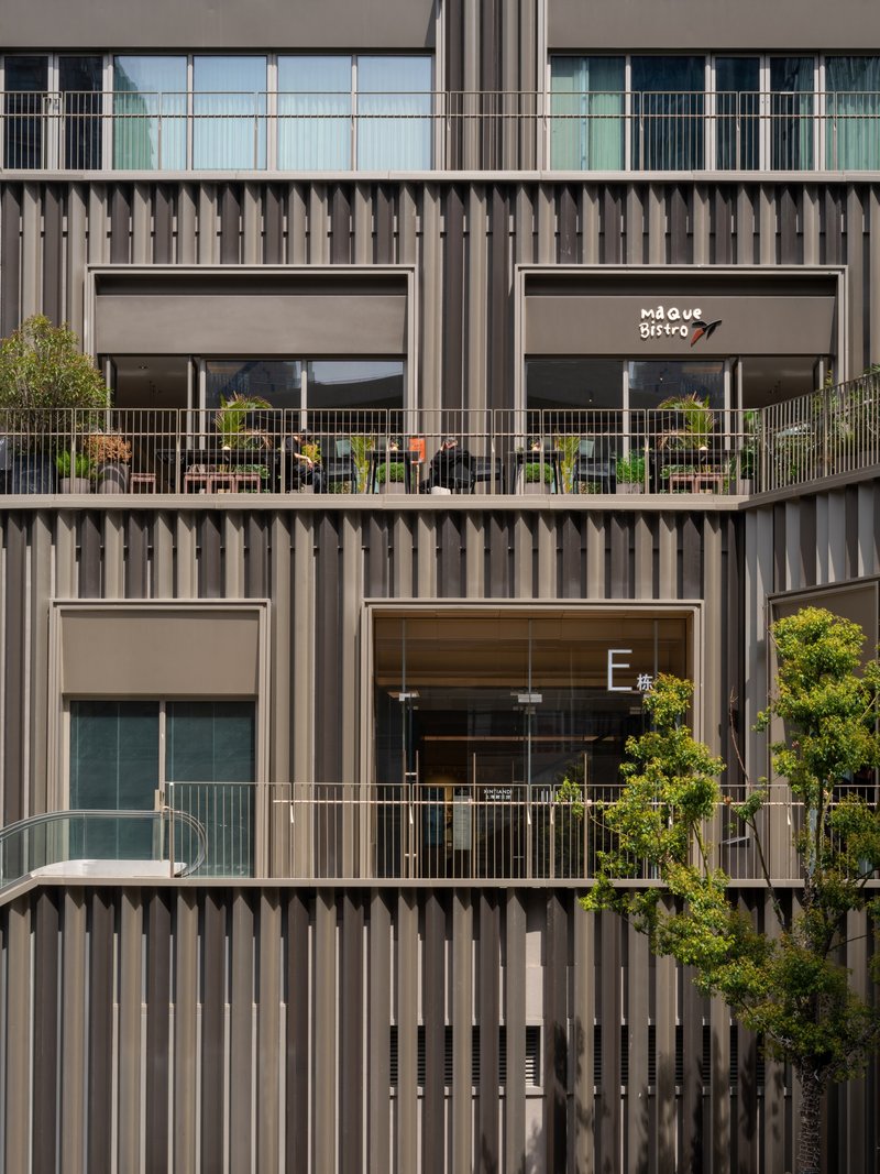 Stacked facade with vertical metal fins, recessed balconies, and potted trees on terrace railings