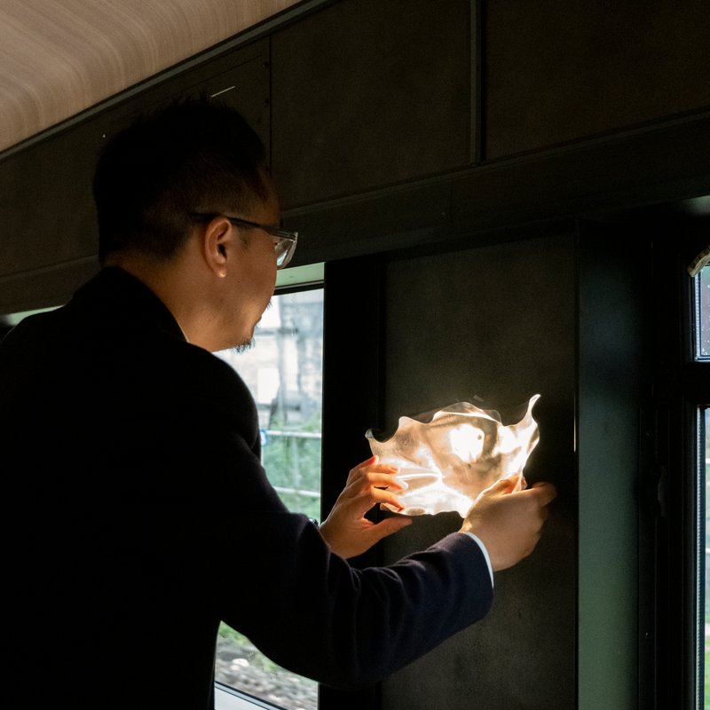 Passenger holding illuminated sculptural light fixture beside train window in darkened interior