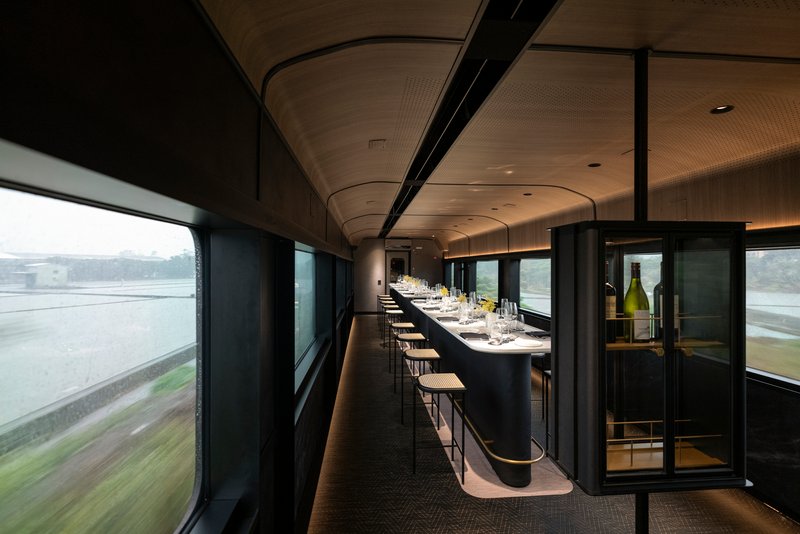 Interior dining car with curved timber ceiling, black banquette seating and landscape blurring past the windows