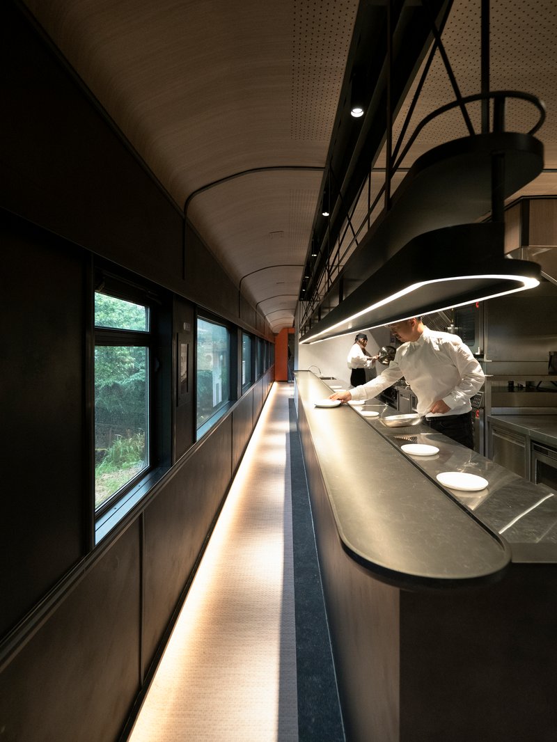 Galley workspace with continuous illuminated counter and chef plating under a curved ring pendant light
