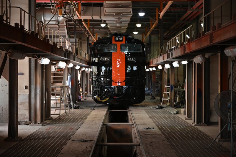 Steam locomotive centered in a maintenance shed with overhead cranes and metal walkways on both sides
