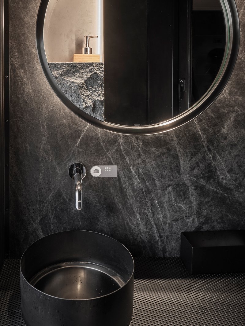 Bathroom vanity with circular backlit mirror above a cylindrical basin and grey marble wall