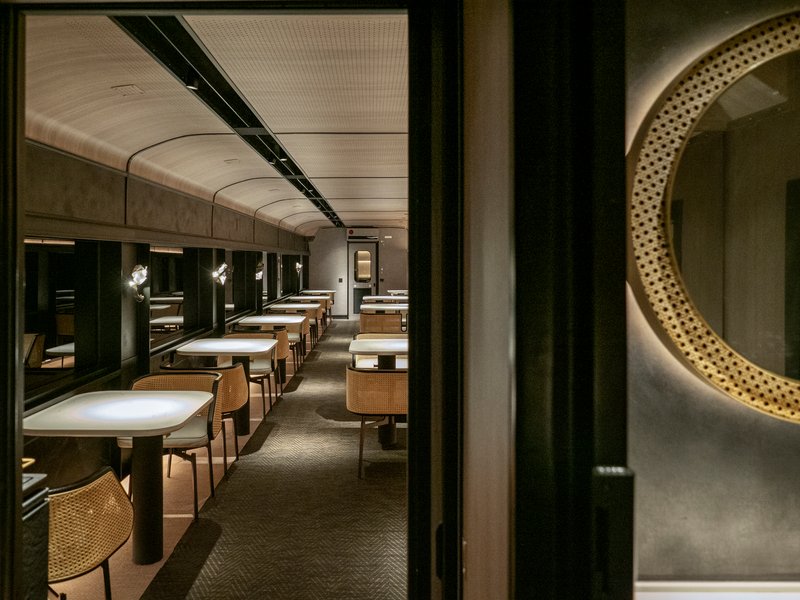 Long view down train dining carriage showing repeated booths beneath curved perforated ceiling