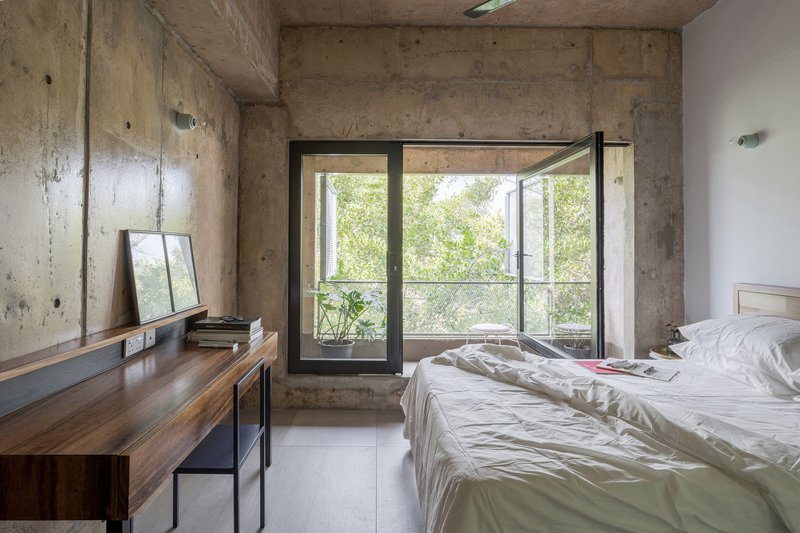 Bedroom with exposed concrete walls and ceiling, open casement window revealing greenery outside