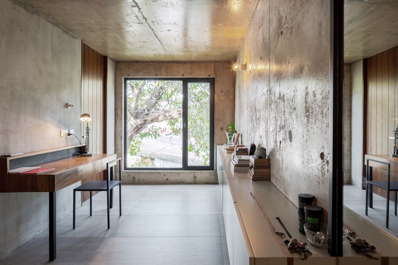 Interior workspace with timber desk, exposed concrete walls and window framing garden views