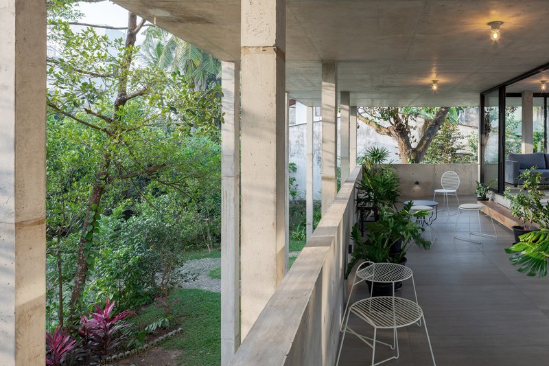 Covered terrace with exposed concrete ceiling and wire chairs opening onto a garden with tropical plants