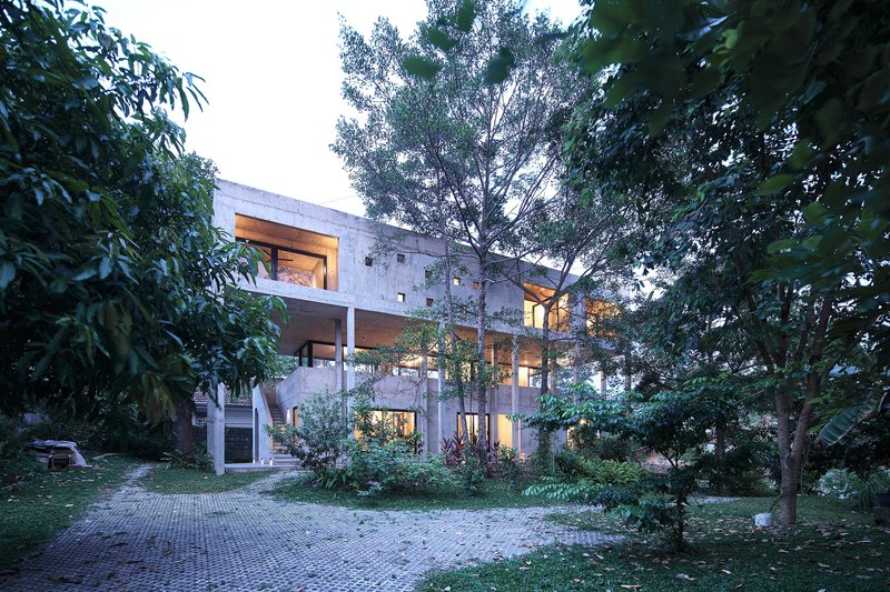 Garden view of the concrete house with recessed balconies amid mature trees at dusk