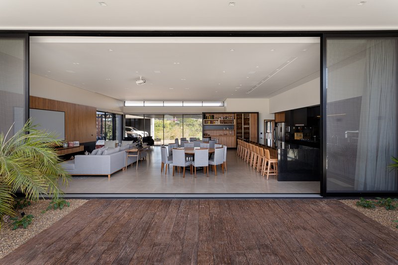 View from the exterior deck through floor-to-ceiling glass showing the open interior with dining area and timber cabinetry